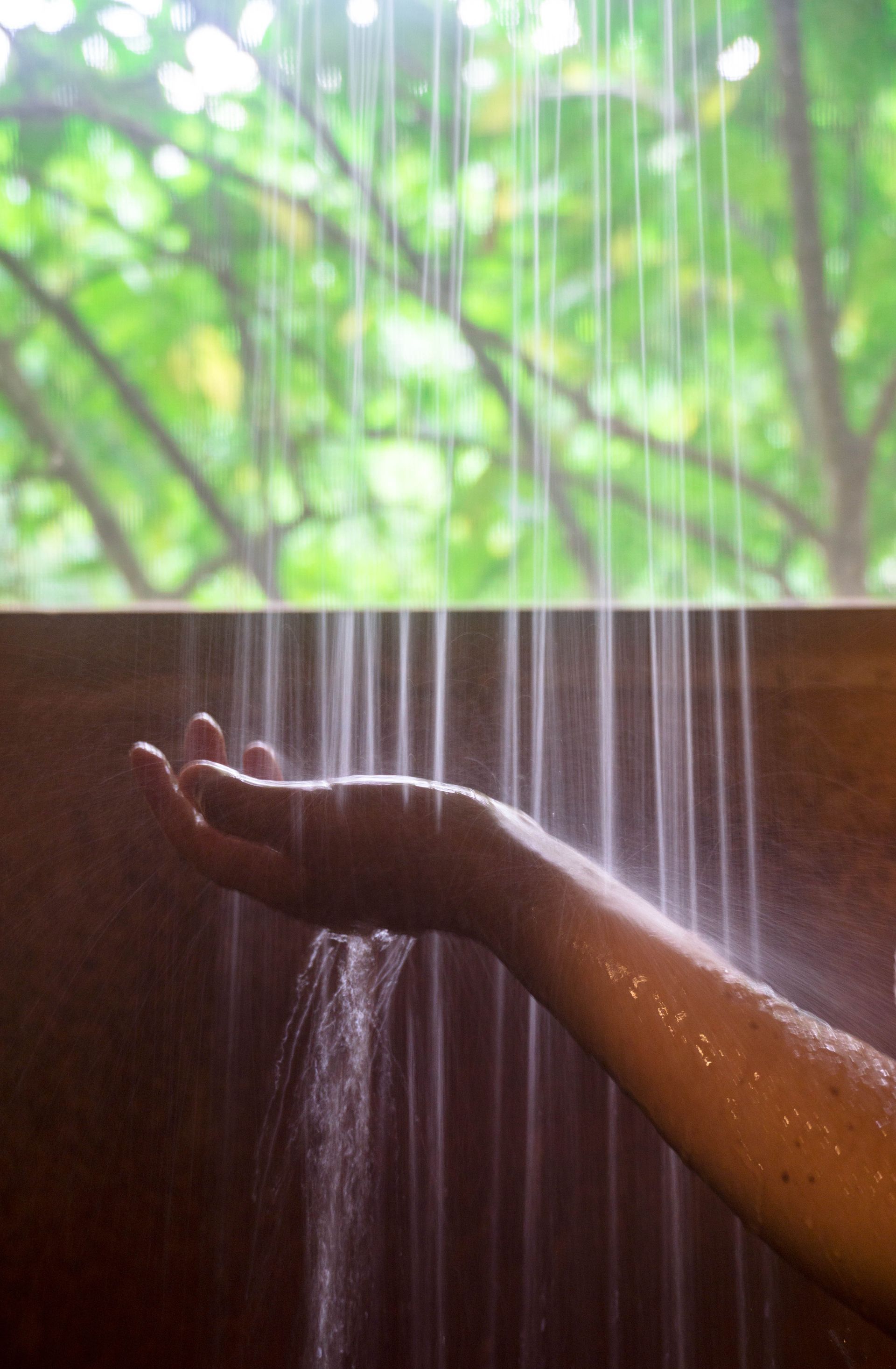 A woman 's hand is reaching out towards a shower head.
