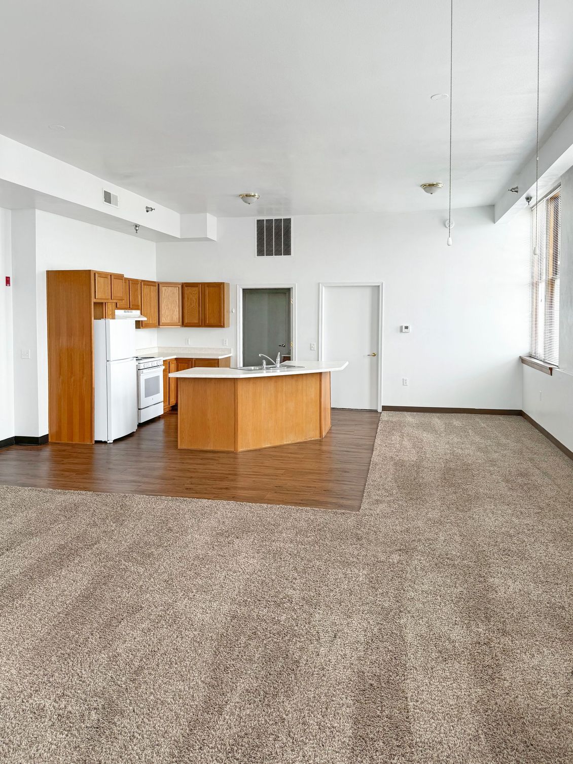 An empty apartment with a kitchen and a large island in the middle of the room.