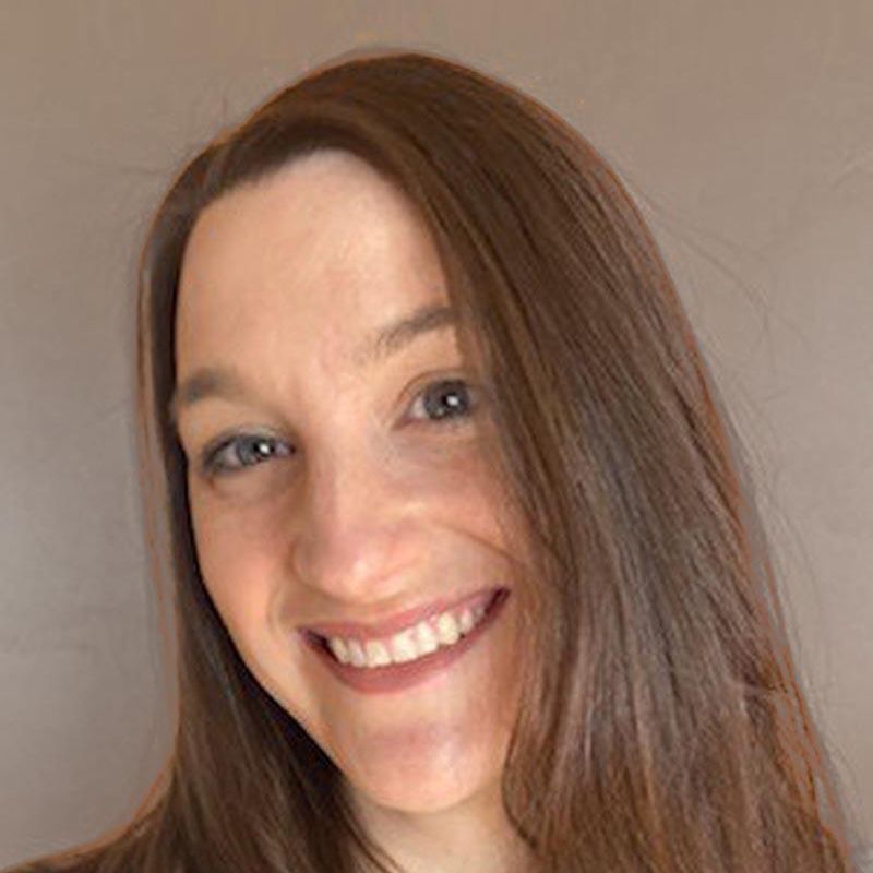Smiling woman with long brown hair against a plain beige background