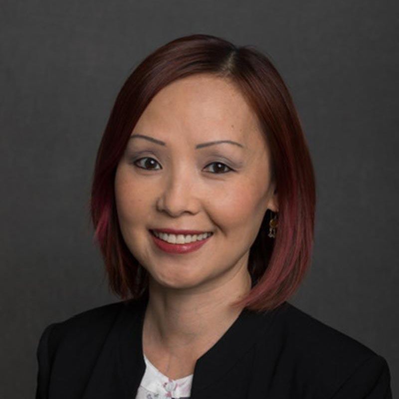 Professional headshot of a smiling person in a black blazer against a gray background