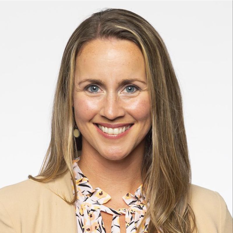 Smiling woman in a beige blazer and patterned blouse against a white background