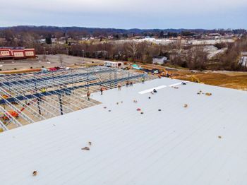 Snow-covered rooftop construction site with steel framing and scattered workers in the distance