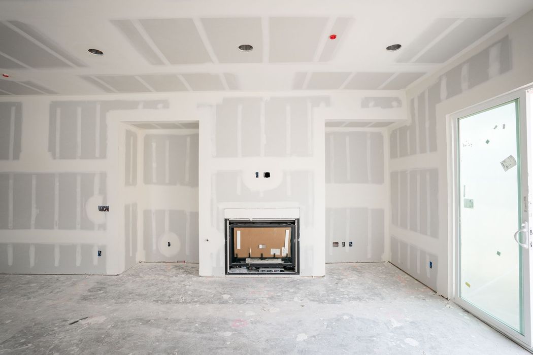 Empty drywall living room with a fireplace, unfinished floor, and a glass door to the right.