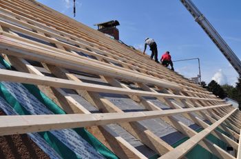 Roof workers installing wooden framing on a steep roof under a blue sky