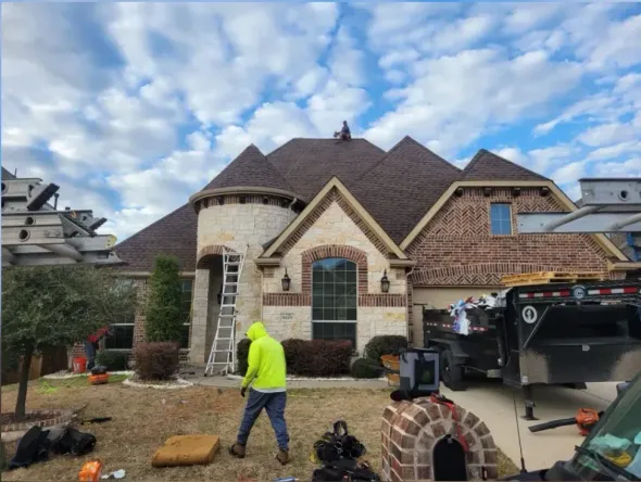 Workers landscaping a brick house exterior with a neon jacketed person and equipment under a cloudy sky