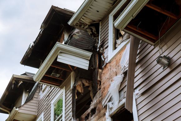 Severely damaged multi-story houses with broken siding and exposed framing after storm damage