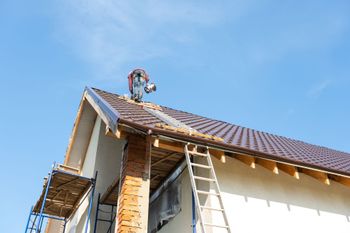 House roof under construction with ladders against a blue sky
