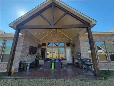 Covered brick entrance with dark columns, string lights, and outdoor seating under a peaked roof.