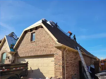 Workers repairing a brick house roof with ladders under a clear blue sky