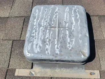 Weathered gray metal utility box on a rooftop, with white residue and a tan mounting bracket.