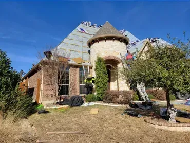 Stone house with a turret and steep roof in a dry yard under a blue sky