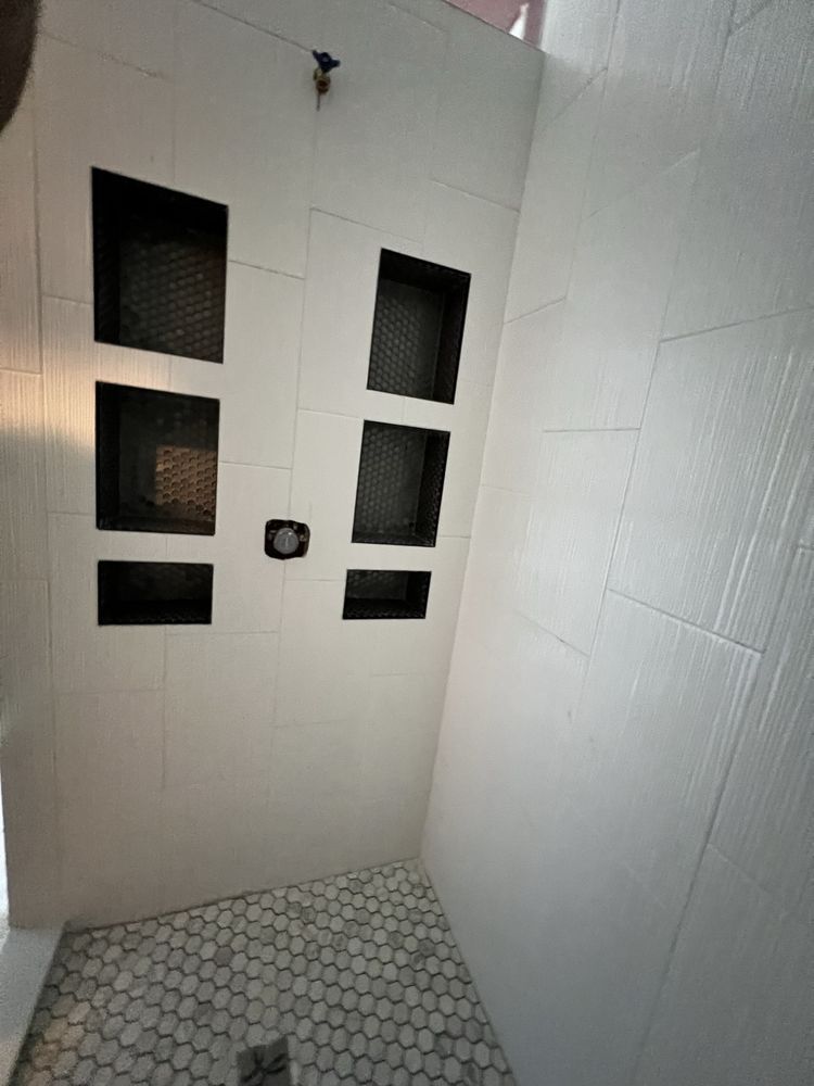 White tiled shower with built-in storage niches, a penny tile floor, and a showerhead.