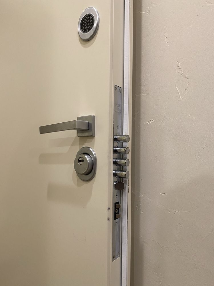 White door with silver hardware: handle, key lock, digital keypad, and multiple bolt locks.