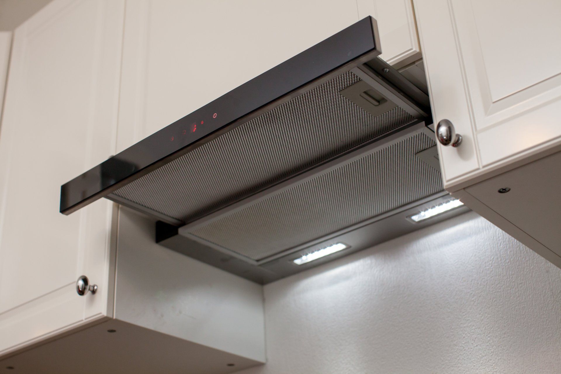 A kitchen hood is hanging from the ceiling above the cabinets.