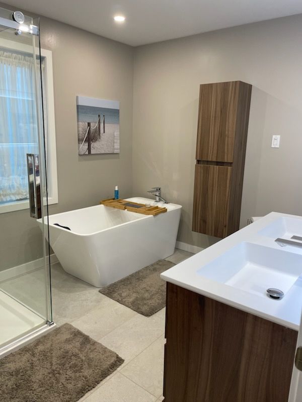 Salle de bains moderne avec baignoire blanche, douche, meuble-lavabo en bois et palette de couleurs neutres.