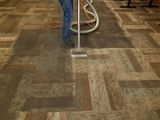 Person vacuuming a patterned carpet with a gray upright vacuum and orange hose