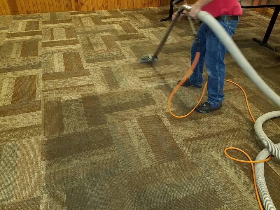 Worker cleaning patterned carpet with a vacuum in a room with wood-paneled walls