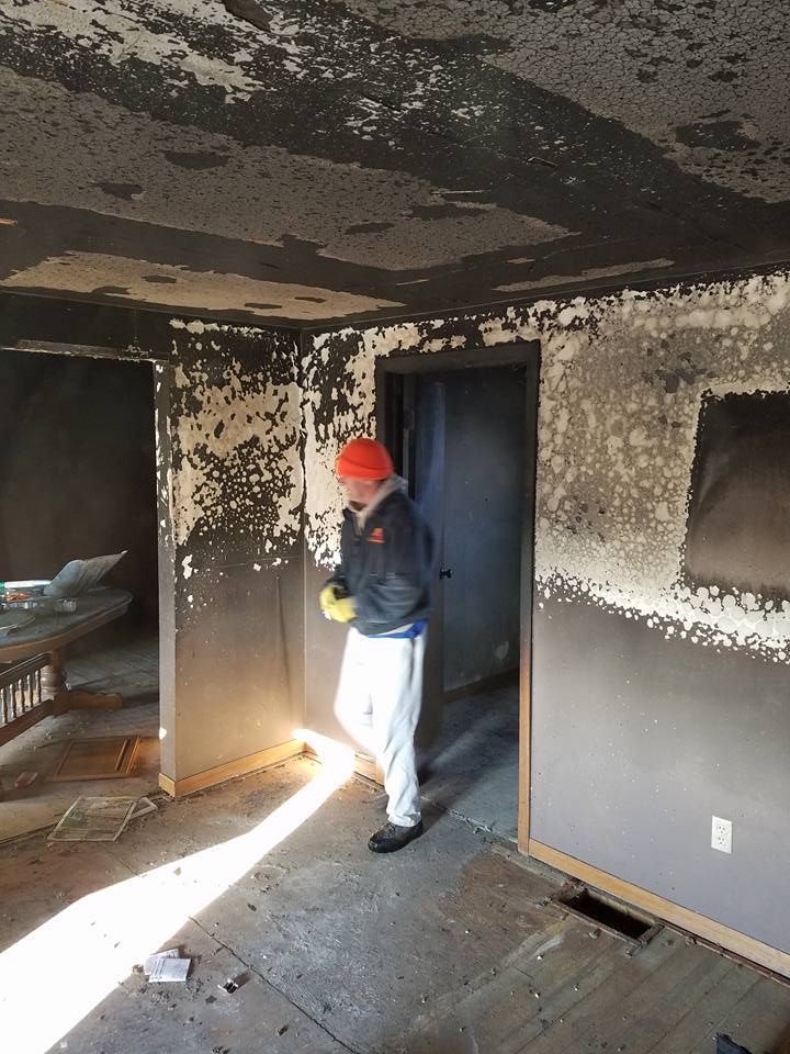 Worker in hard hat inspecting a charred room with damaged walls and ceiling under renovation