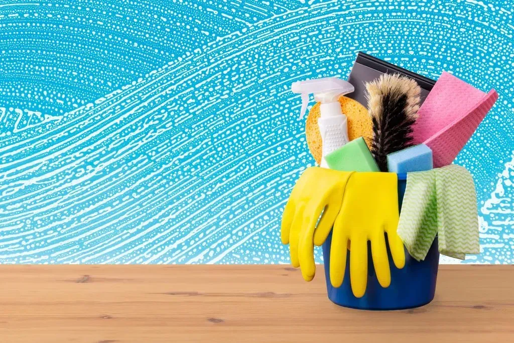 Cleaning tools in a blue bucket on a wooden table against a blue background
