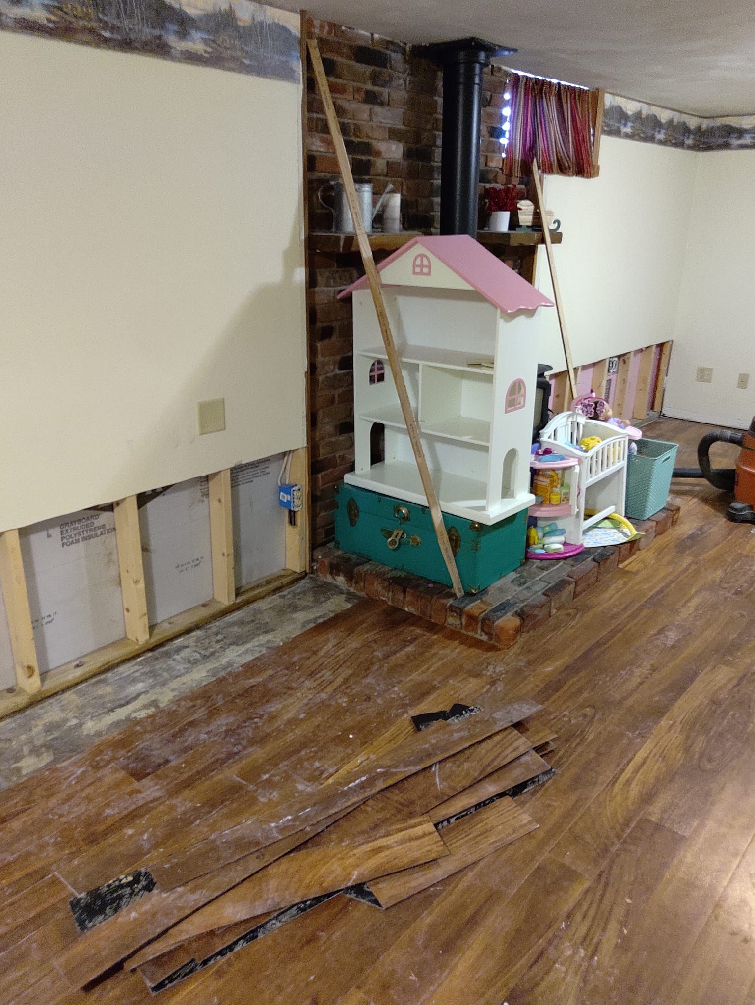 Partially stripped room with exposed walls, wood floor, and a child’s toy house and ladder in the corner
