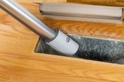 Vacuum cleaner hose cleaning dust from a dark floor strip on a wooden surface