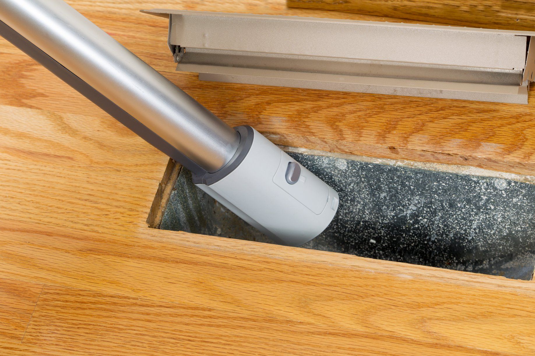 Vacuum cleaner hose cleaning dust from a dark floor strip on a wooden surface