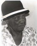 A black-and-white portrait of a person wearing a dark hat with a light-colored band and a patterned shirt.