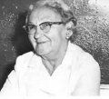 A person wearing glasses and a collared white shirt, smiling slightly while looking toward the left.