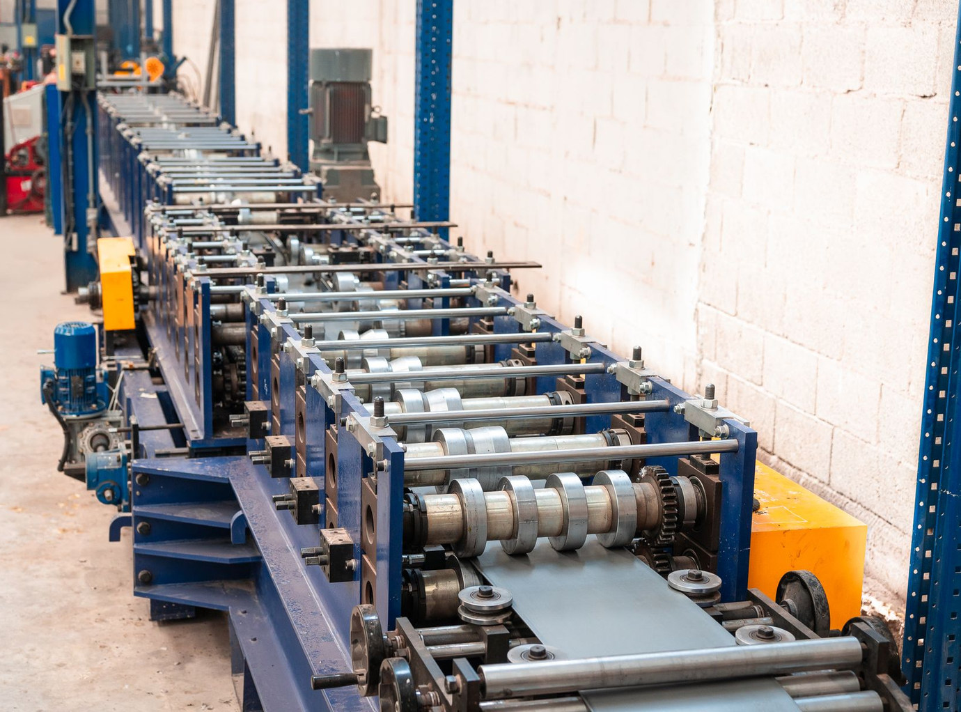 Primer plano de una máquina laminadora de metal con piezas cilíndricas giratorias en un entorno industrial.