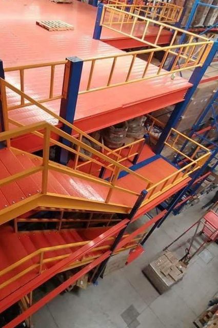 Escalera industrial multinivel de color rojo y amarillo con barandillas de seguridad en el interior de un almacén.