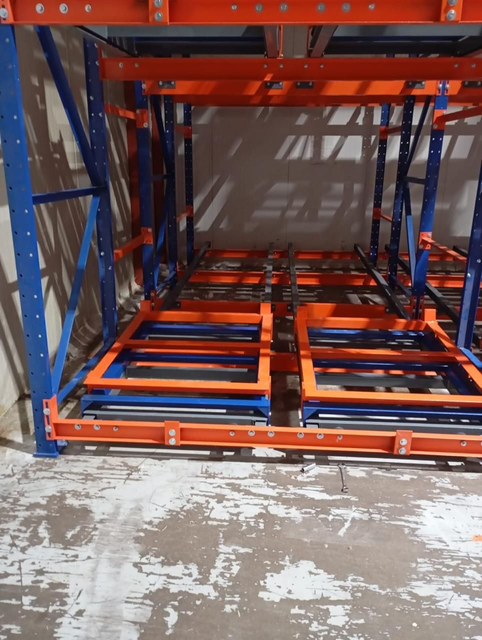 Estantería metálica azul y naranja de almacén con plataformas inferiores vacías en un área de almacenamiento.
