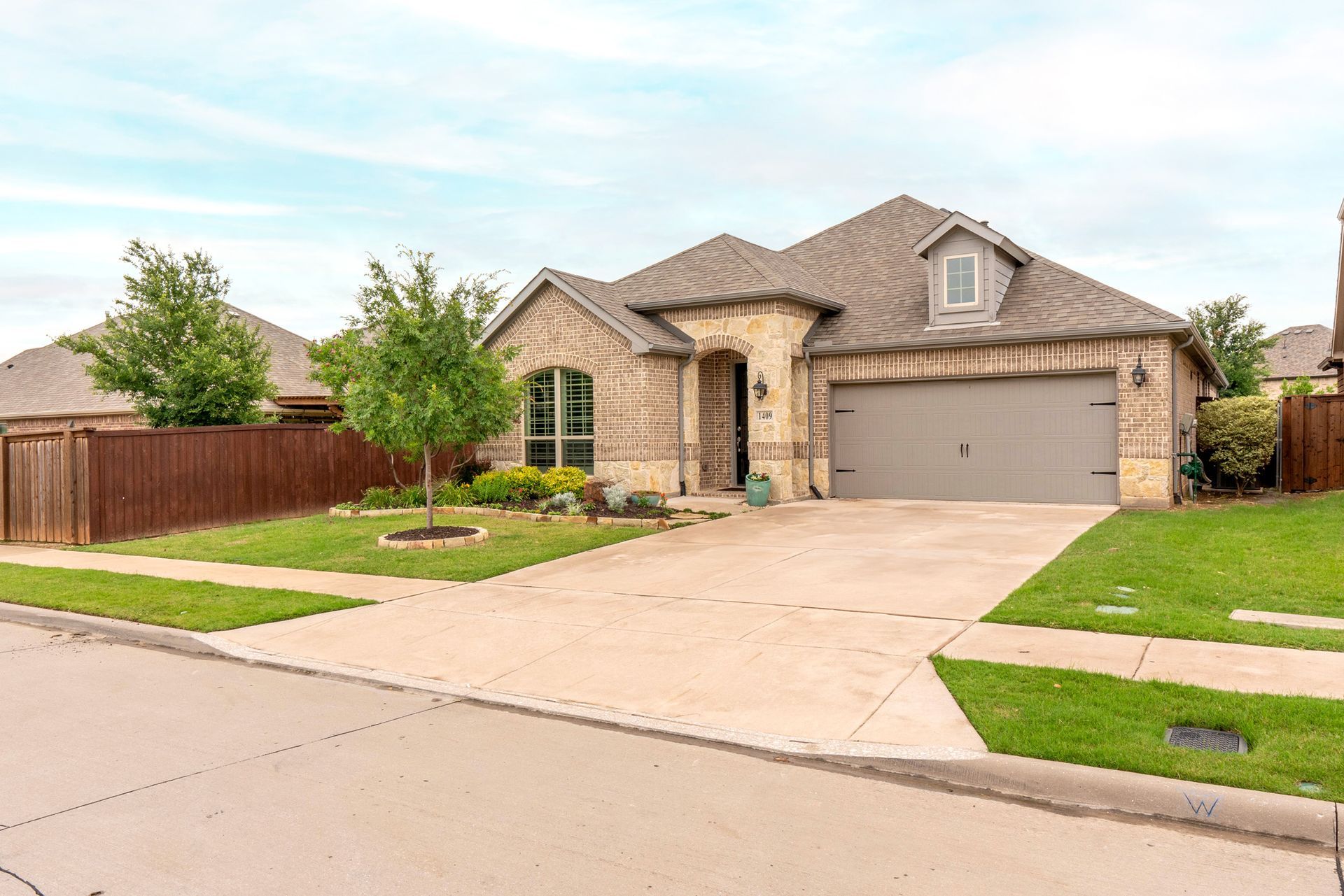 Suburban brick house with a two-car garage, driveway, and manicured front lawn