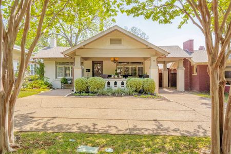 Single-story bungalow with a wide front porch, framed by trees and a brick driveway