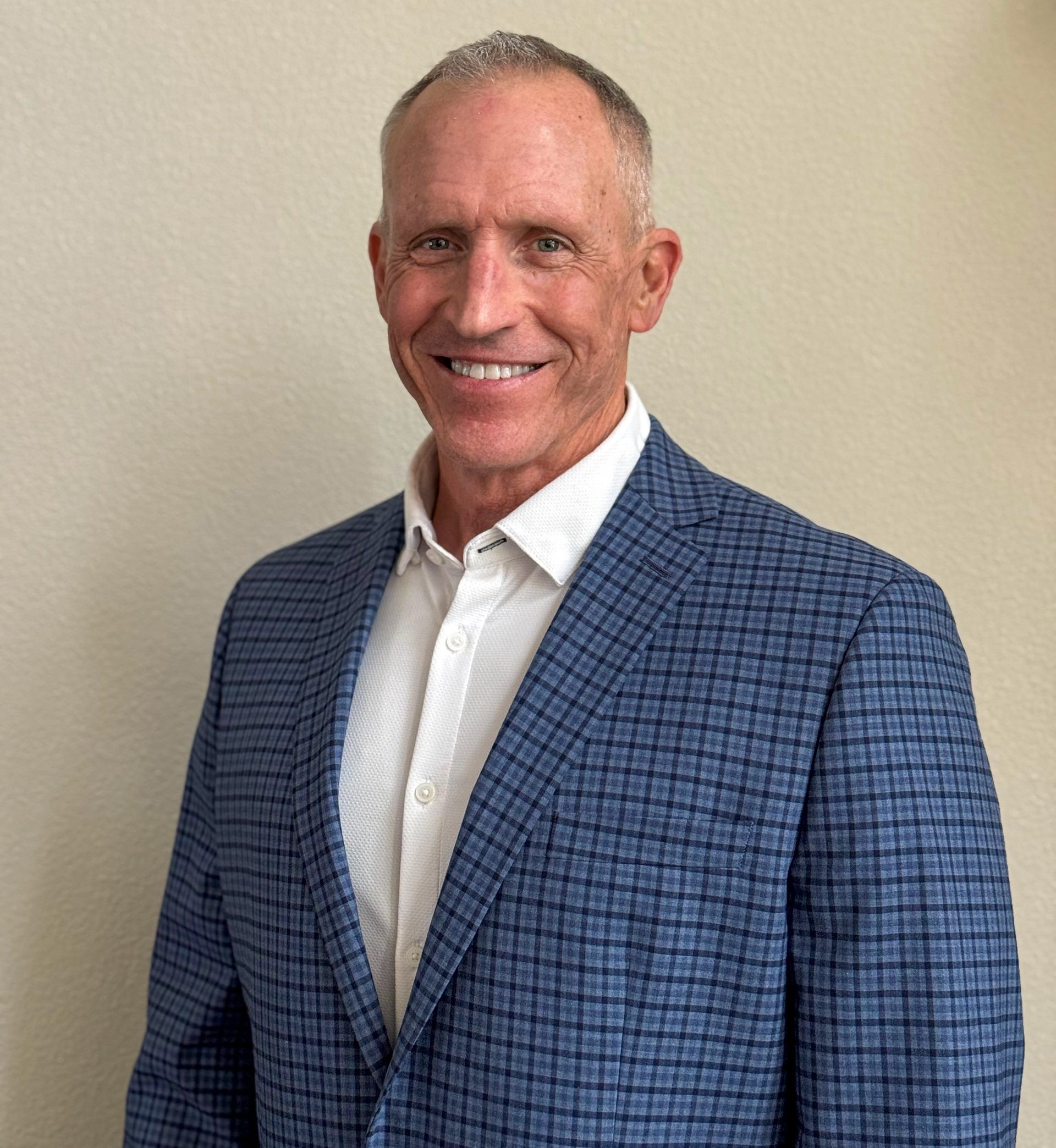 Smiling man in a blue checkered blazer and white shirt against a beige background