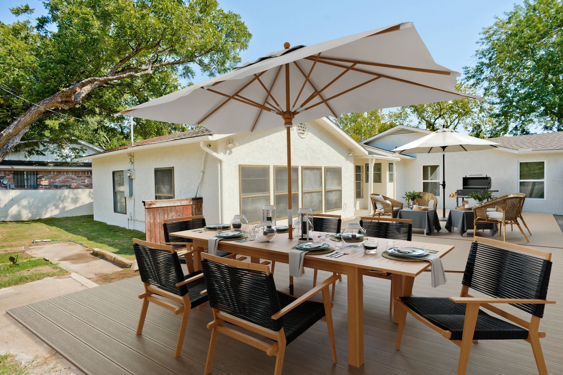 Outdoor patio dining area with wooden tables, chairs, and a large umbrella beside a house