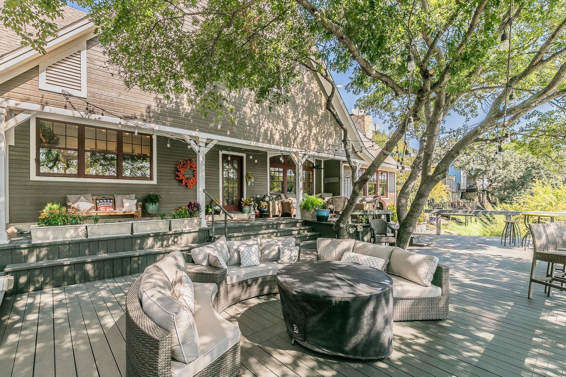 Outdoor patio dining area with wooden tables, chairs, and a large umbrella beside a house