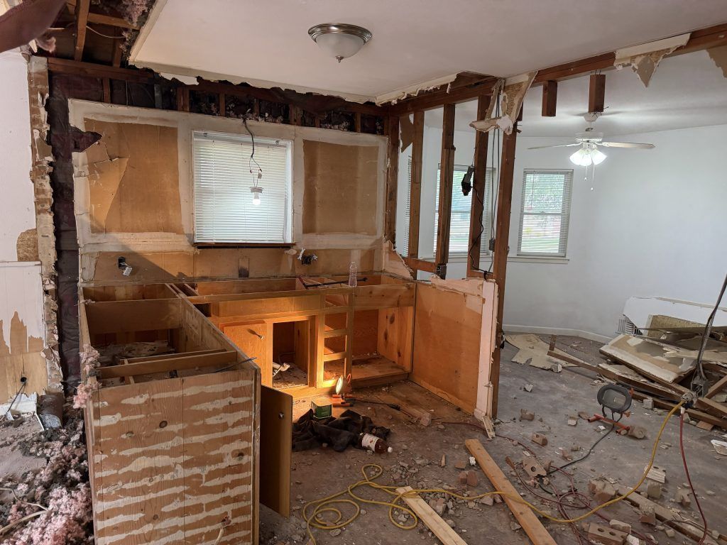 Damaged kitchen interior with exposed studs, broken cabinets, and debris on the floor