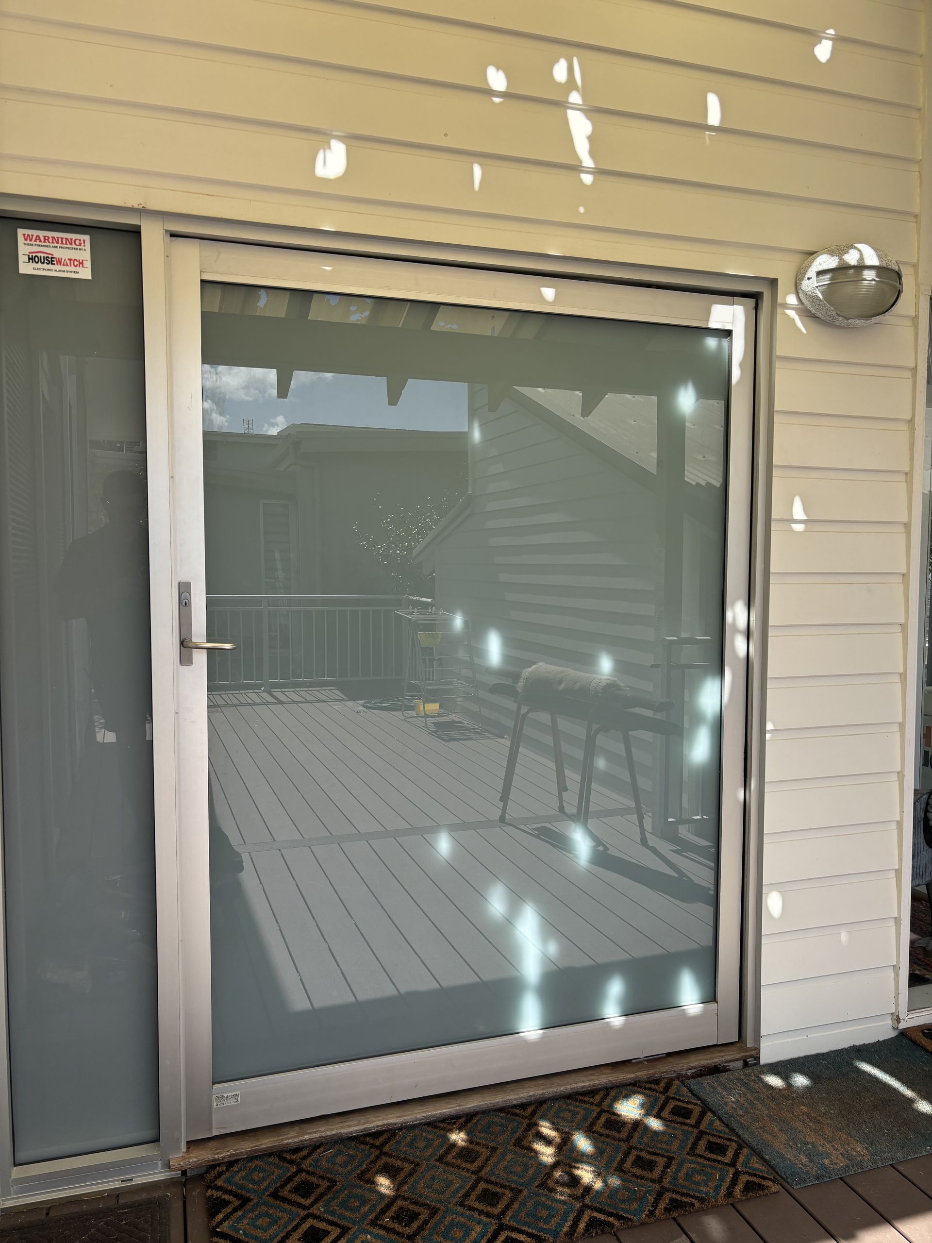 Sliding glass door with screen, leading to a patio with a grill. Beige siding surrounds the door-Fix-A-Door in Morisset, NSW
