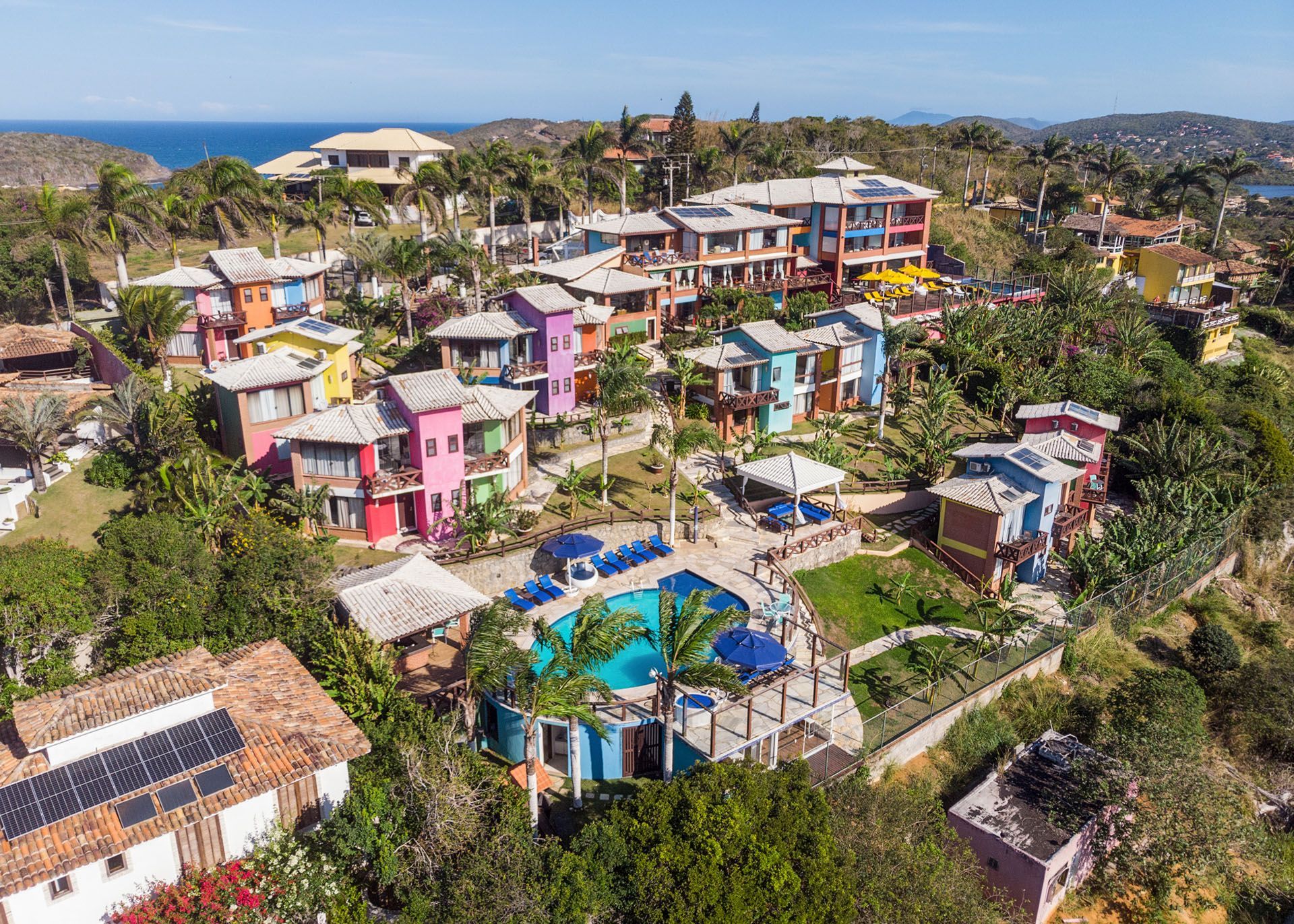 Resort colorido na encosta, com vilas, piscinas e vegetação tropical com vista para o oceano.