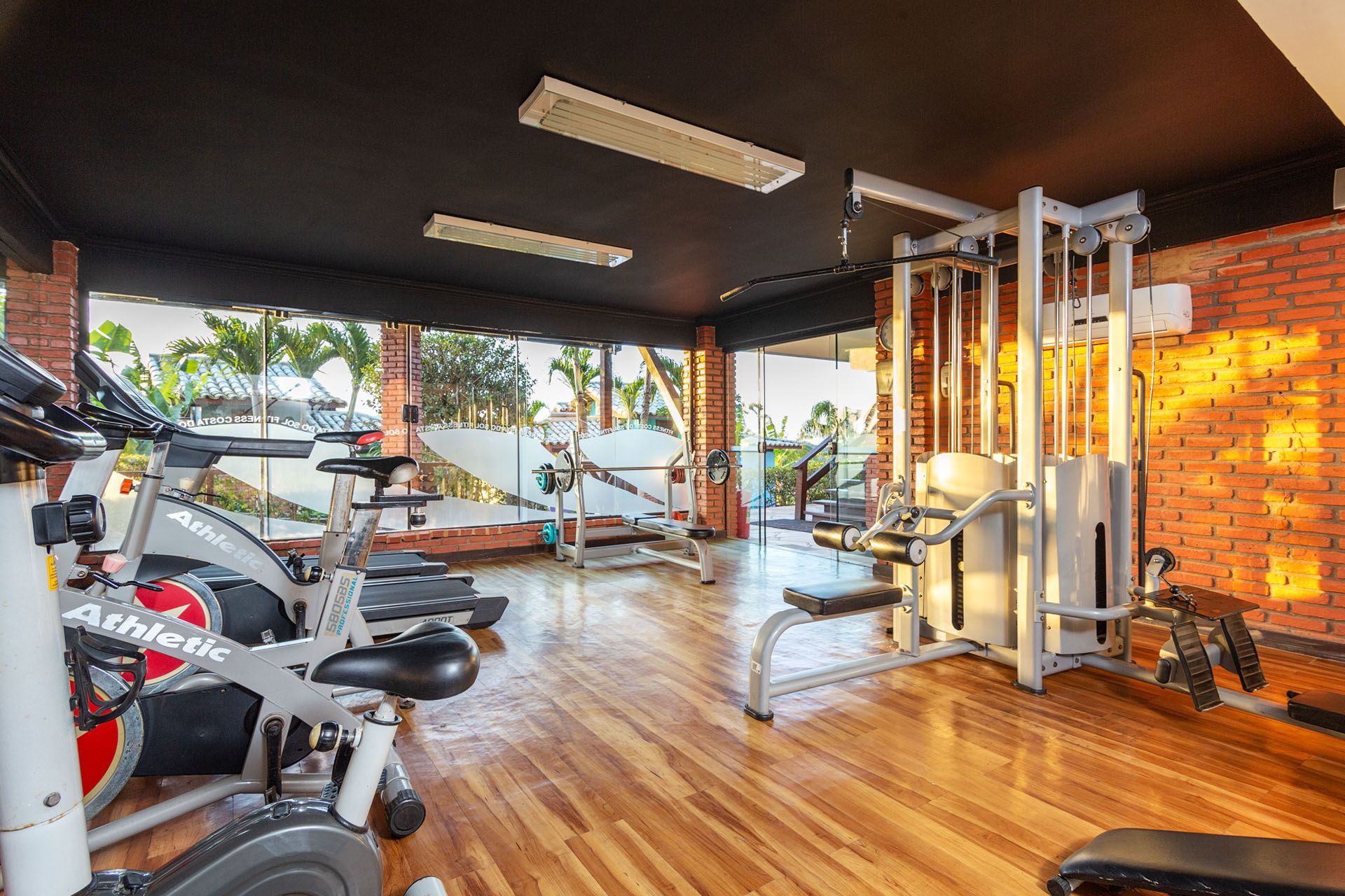 Interior de academia moderna com bicicletas ergométricas, aparelhos de musculação e piso de madeira sob iluminação aconchegante.