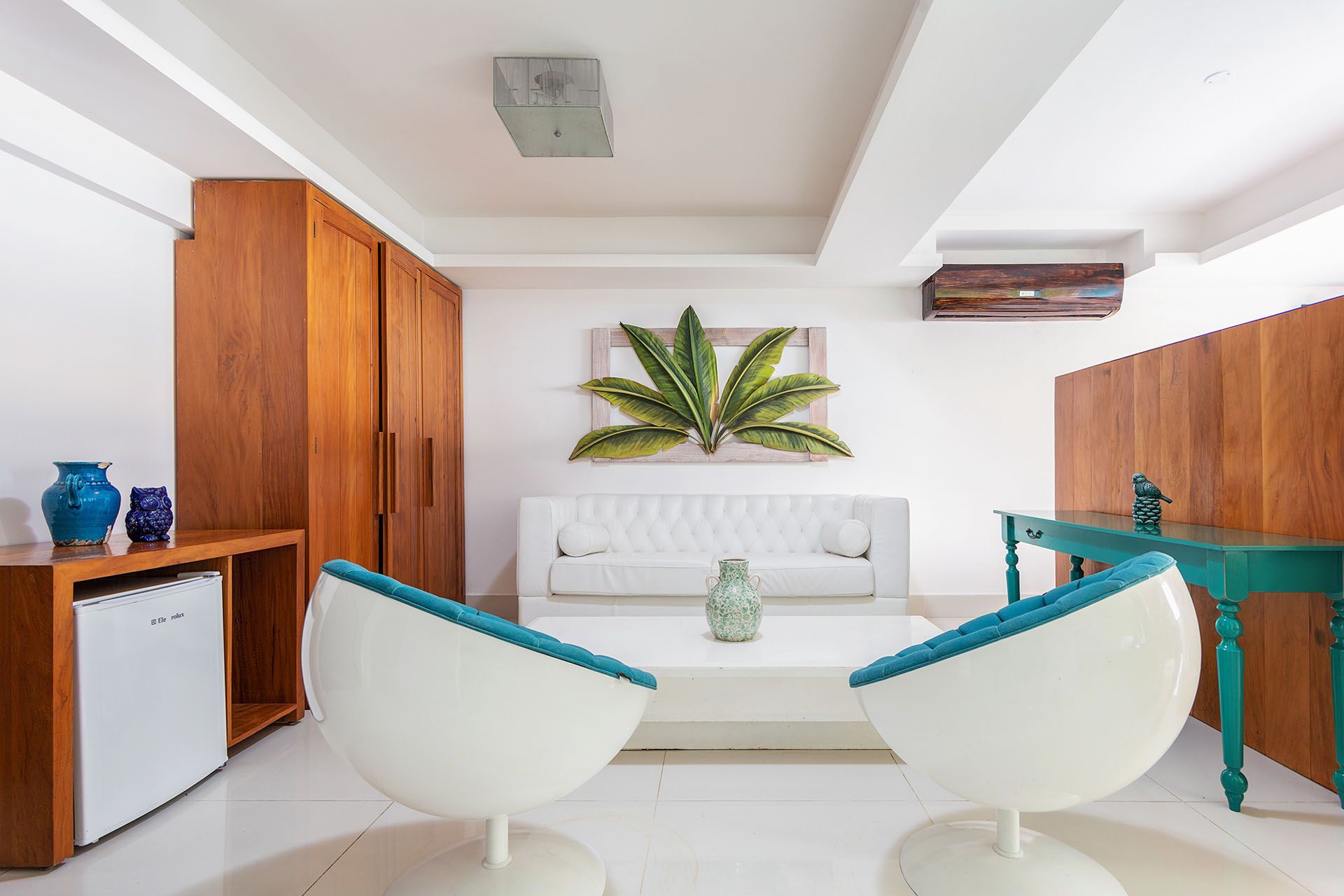 Sala de estar moderna branca com duas cadeiras curvas, sofá branco, armários de madeira e detalhes em azul-petróleo.