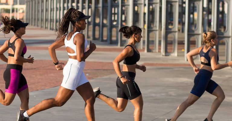 Quatro mulheres com roupas esportivas correndo ao ar livre.
