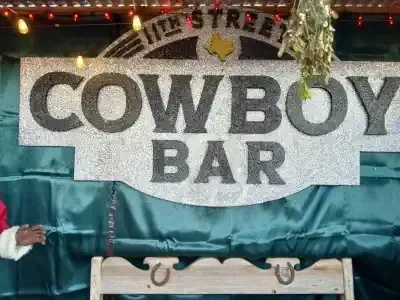 COWBOY BAR sign with large black letters on a white backdrop, lit by string lights