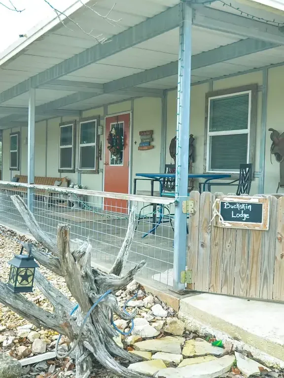 Front porch of a rustic lodge with an orange door, white railing, and a “Lush Cabin Lodge” sign.
