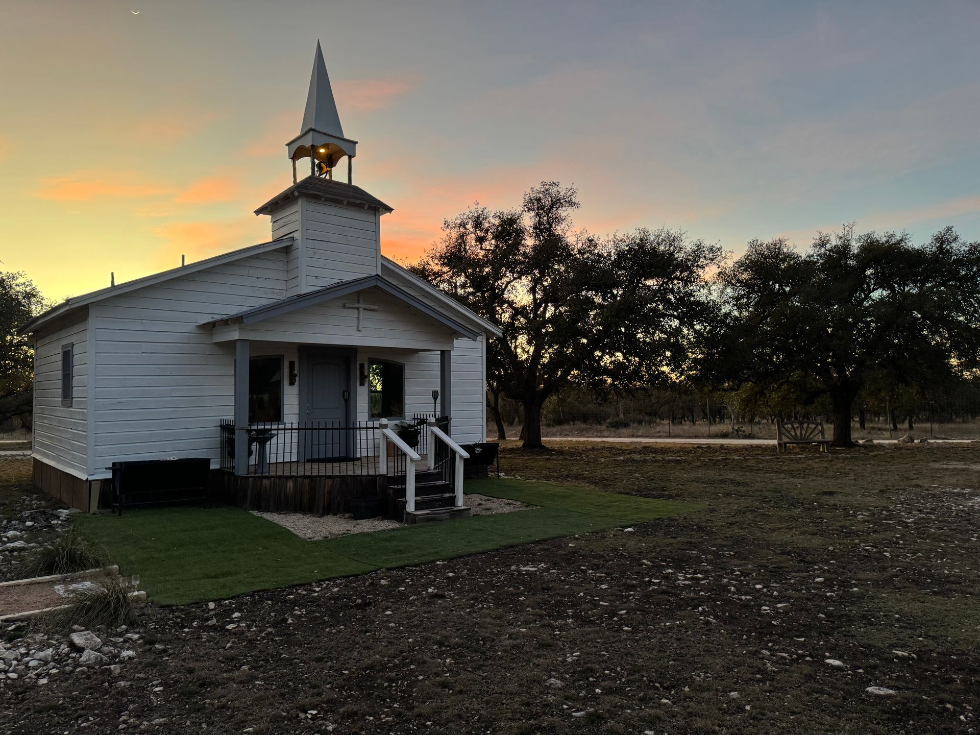 Small white church with steeple at sunset, beside trees and an open field