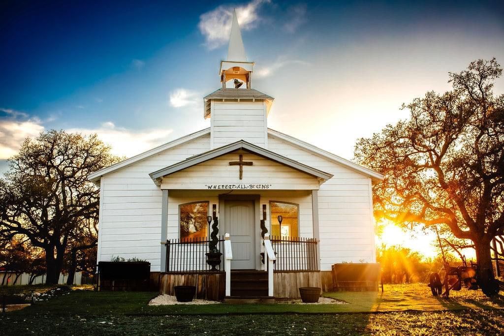 White church at sunset with golden light, front porch, and leafless trees on either side