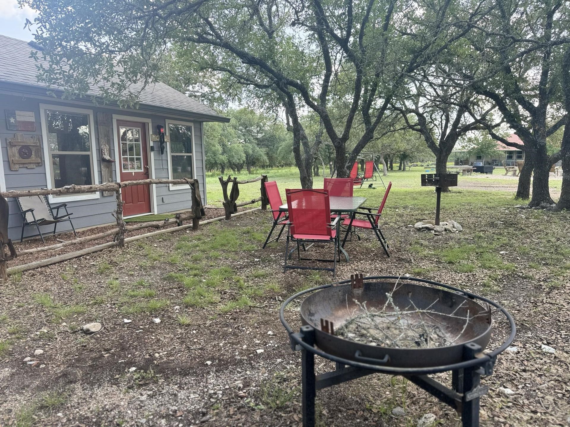 Backyard fire pit and red patio chairs beside a small shed under large trees