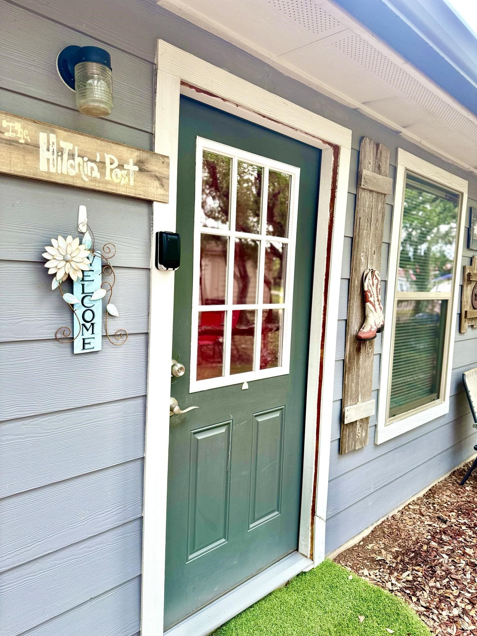 Front porch with a teal door, white trim, and a wooden sign beside light blue siding.