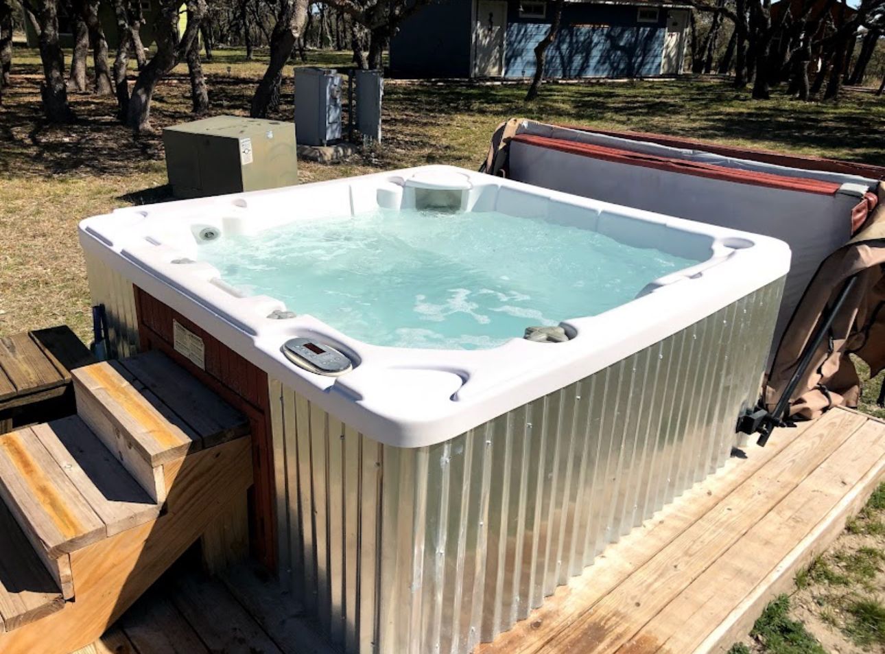 Outdoor hot tub on a wooden deck, filled with bubbling water and surrounded by trees.