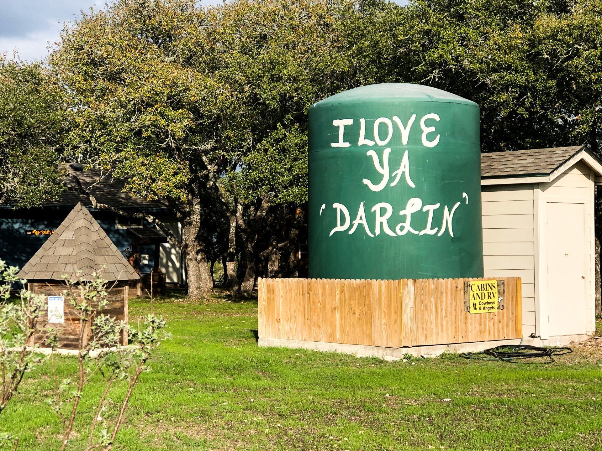 Green tank with “I LOVE YA DARLIN’” painted on it beside a small shed in a grassy yard